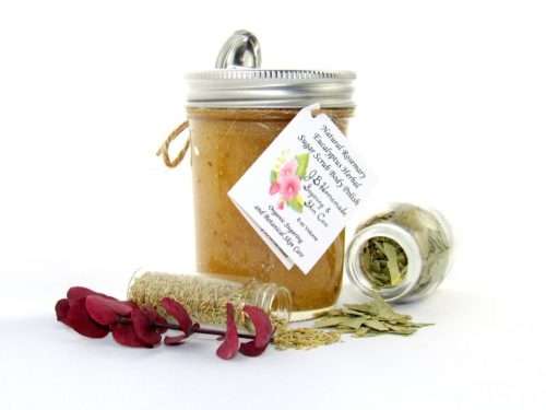 An 8 oz jar of refreshing herbal cane sugar scrub is infused with rosemary and eucalyptus, perfect for rejuvenating weary skin. The accompanying image shows the scrub jar centrally placed, flanked by two smaller glass jars—one filled with dried rosemary, the other with dried eucalyptus—both tipped over, their contents scattered on a pristine white surface. Beside the jar lies a sprig of dried eucalyptus.