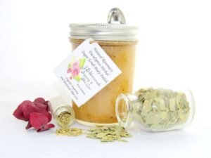 An 8 oz jar of refreshing herbal cane sugar scrub is infused with rosemary and eucalyptus, perfect for rejuvenating weary skin. The accompanying image shows the scrub jar centrally placed, flanked by two smaller glass jars—one filled with dried rosemary, the other with dried eucalyptus—both tipped over, their contents scattered on a pristine white surface. Beside the jar lies a sprig of dried eucalyptus.