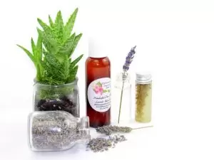 Lavender Serenity Aloe – Handcrafted Lavender-Infused Aloe Vera (2 oz) A 2 oz bottle of JBHomemade's handcrafted lavender-infused aloe vera, crafted with natural and homegrown lavender buds and aloe vera, is paired with an aloe vera plant. Alongside, a glass jar brimming with lavender buds spills over, and a small glass jar contains a sprig of lavender steeping in pure aloe vera, with two lavender sprigs resting to the right.