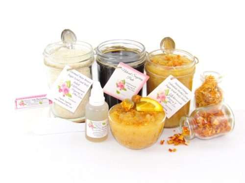 A collection of skincare products including an 8 oz mason jar of sugaring paste, Orange Calendula Herbal Sugar Scrub, and Colloidal Oatmeal Brown Sugar Dry Body Scrub, accompanied by smaller jars of calendula petals and dried orange zest on a white background.