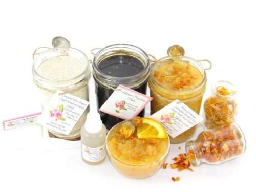 A collection of skincare products including an 8 oz mason jar of sugaring paste, Orange Calendula Herbal Sugar Scrub, and Colloidal Oatmeal Brown Sugar Dry Body Scrub, accompanied by smaller jars of calendula petals and dried orange zest on a white background.