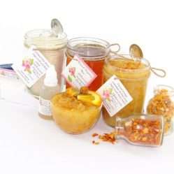 A collection of skincare products including an 8 oz mason jar of sugaring wax, Orange Calendula Herbal Sugar Scrub, and Colloidal Oatmeal Brown Sugar Dry Body Scrub, a small bottle of pure aloe vera, a pouch of cornstarch, denim strips, an applicator, accompanied by smaller jars of calendula petals and dried orange zest on a white background.