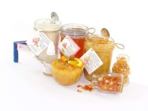 A collection of skincare products including an 8 oz mason jar of sugaring wax, Orange Calendula Herbal Sugar Scrub, and Colloidal Oatmeal Brown Sugar Dry Body Scrub, a small bottle of pure aloe vera, a pouch of cornstarch, denim strips, an applicator, accompanied by smaller jars of calendula petals and dried orange zest on a white background.