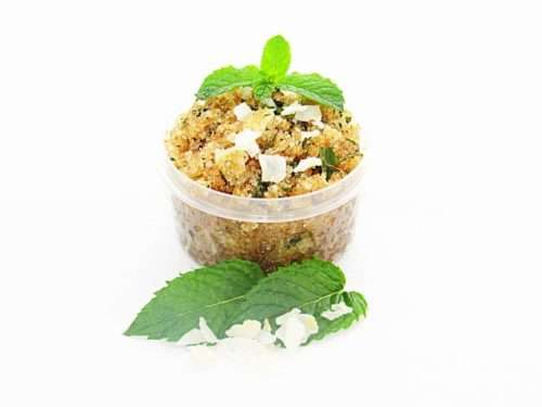 A 2 oz tub of cooling peppermint and coconut cane sugar scrub offers a refreshing and hydrating experience for your skin. The sugar scrub tub is centrally placed, flanked by bright green sprigs of peppermint and coconut flakes are scattered throughout the arrangement.