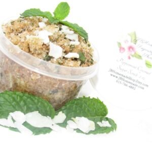 A 2 oz tub of cooling peppermint and coconut cane sugar scrub offers a refreshing and hydrating experience for your skin. The sugar scrub tub is centrally placed, flanked by bright green sprigs of peppermint and coconut flakes are scattered throughout the arrangement.