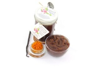 Indulge in the seasonal warmth of an 8 oz jar of pumpkin vanilla brown sugar scrub. The jar is prominently displayed at the center, accompanied by a glass bowl showcasing the scrub's rich texture. To the left, a smaller bowl contains pure pumpkin puree and a whole vanilla bean, highlighting the scrub's natural ingredients.