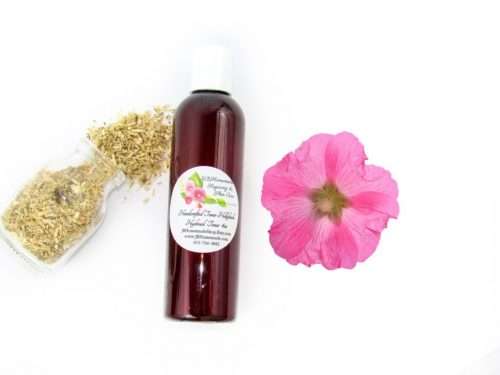 A bottle of JBHomemade’s handcrafted hollyhock water toner, made with organic marshmallow root and fresh hollyhock blooms, accompanied by dried marshmallow root and a vibrant hollyhock flower.