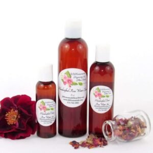 Three sizes of handcrafted rose water bottles displayed with a fresh red rose on the left and dried roses spilled from a glass jar on the right. The collection showcases the natural and organic essence of JBHomemade’s garden-fresh rose water.