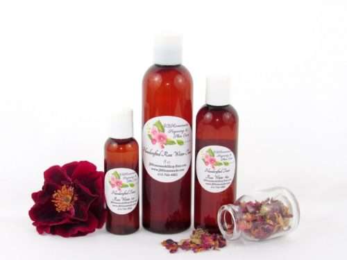 Three sizes of handcrafted rose water bottles displayed with a fresh red rose on the left and dried roses spilled from a glass jar on the right. The collection showcases the natural and organic essence of JBHomemade’s garden-fresh rose water.