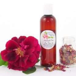 A 4 oz bottle of handcrafted rose water is presented with a vibrant red rose to the left and dried rose petals scattered from a glass jar on the right, capturing the pure and organic quality of JBHomemade's garden-fresh rose water.