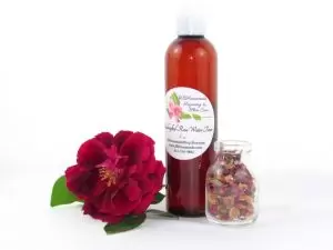 Pure Handcrafted Rose Water – 8 oz Bottle An 8 oz bottle of handcrafted rose water is presented with a vibrant red rose to the left and dried rose petals scattered from a glass jar on the right, capturing the pure and organic quality of JBHomemade's garden-fresh rose water. Right Perspective.