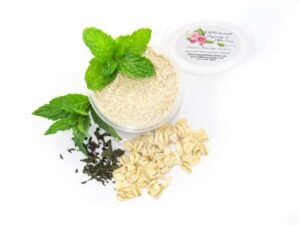 Discover a 2 oz tub of gentle exfoliating dry body scrub, ideal for sensitive skin, featuring colloidal oatmeal, fresh and dried mint, and brown sugar. Accompanying the scrub are oats and dried mint artfully spilled on a white table, complemented by sprigs of bright green fresh mint.
