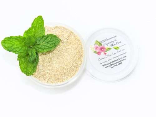 Discover a 2 oz tub of gentle exfoliating dry body scrub, ideal for sensitive skin, featuring colloidal oatmeal, fresh and dried mint, and brown sugar, complemented by sprigs of bright green fresh mint.