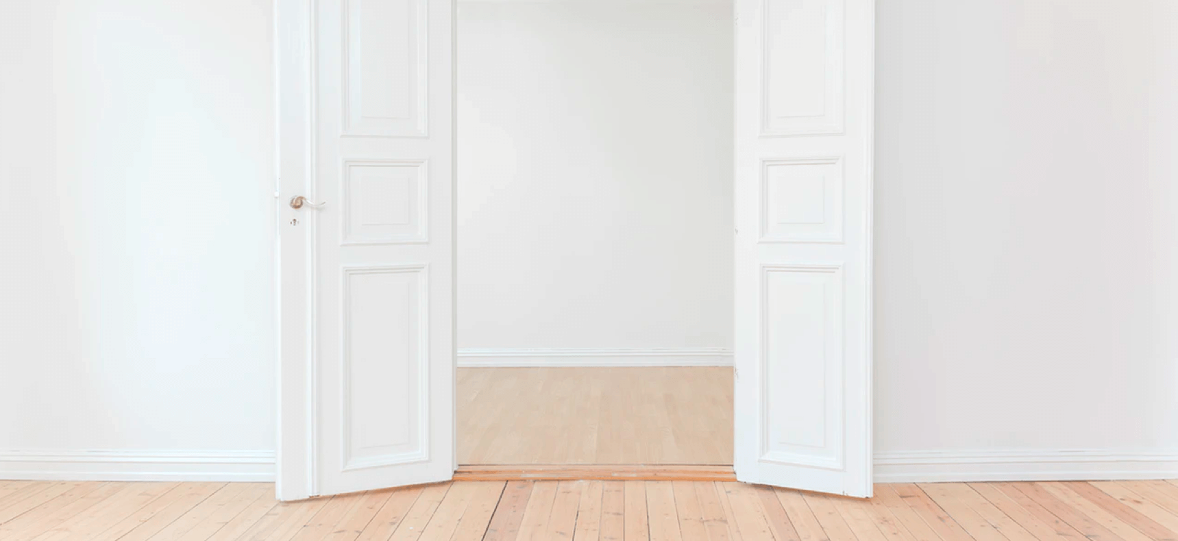A pair of elegant white doors opened to reveal a warm, inviting wooden floor, symbolizing a welcoming entrance.
