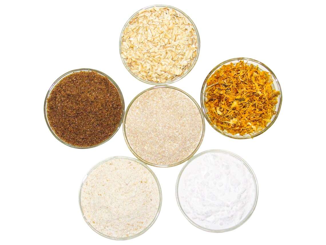 A selection of natural ingredients including whole oats, brown sugar, colloidal oatmeal, baking soda, and calendula for the Calendula Oatmeal Bath Soak, displayed in separate bowls to highlight their purity and quality.