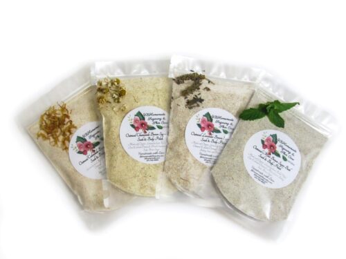 Four sealed packets of herbal bath soaks displayed side by side, each filled with a different type of organic bath soak - calendula with yellow petals on the left, chamomile with chamomile petals in the second position, lavender with purple lavender buds in the third position, and mint with green mint leaves on the right.
