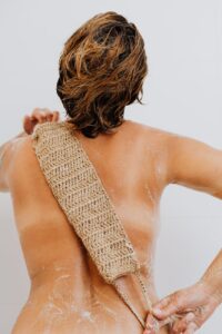 A person scrubbing their back with an exfoliating mitt, emphasizing the importance of routine skin exfoliation after sugaring for optimal skin health.