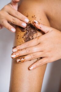 A person applying brown sugar scrub to exfoliate the skin, promoting better sugaring results and improved skin health.