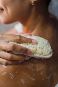 A close-up photo of a person using a loofah, emphasizing the importance of skin exfoliation for optimal sugaring results and overall skin health. Remember to cleanse the skin from oils before sugaring.