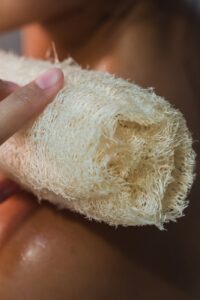 A person holding a loofah, emphasizing the importance of skin exfoliation for optimal sugaring results and overall skin health. Remember to cleanse the skin from oils before sugaring.