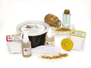 A 16-ounce tub of JBHomemade Sugaring Paste is presented with its included pouches of cornstarch, bottles of aloe vera and applicators next to a slice of fresh lemon, a glass jar filled with clear blue water, and another jar tipped over, spilling raw sugar, accentuating the natural ingredients.