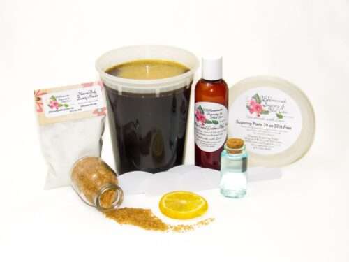 A 32 oz tub of JBHomemade Sugaring Paste is presented with its included large pouch of cornstarch and arrowroot powder, bottle of aloe vera and applicators next to a slice of fresh lemon, a glass jar filled with clear blue water, and another jar tipped over, spilling raw sugar, accentuating the natural ingredients.