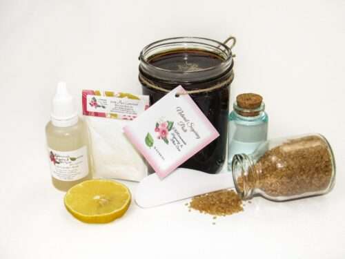 An 8-ounce jar of JBHomemade Sugaring Paste is presented with its included pouch of cornstarch, bottle of aloe vera and applicator next to a slice of fresh lemon, a glass jar filled with clear blue water, and another jar tipped over, spilling raw sugar, accentuating the natural ingredients.