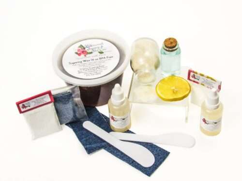A 16-ounce tub of JBHomemade Sugaring Wax is presented with its included pouches of cornstarch, bottles of aloe vera, denim strips and applicators next to a slice of fresh lemon, a glass jar filled with clear blue water, and another jar tipped over, spilling cane sugar, accentuating the natural ingredients.