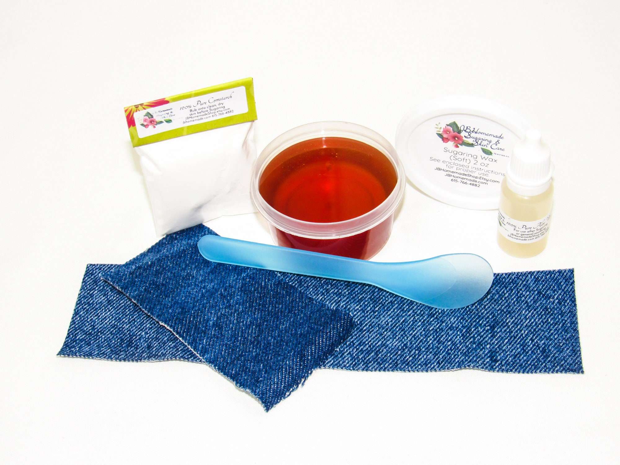 A 2-ounce tub of JBHomemade Sugaring wax is presented with its included pouch of cornstarch, denim strips, bottle of aloe vera and applicator.