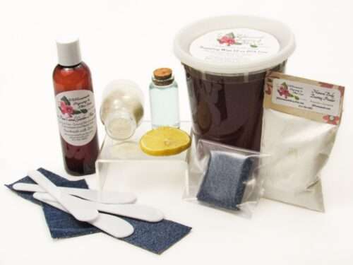 A 32 oz tub of JBHomemade Sugaring Wax is presented with its included large pouch of cornstarch and arrowroot powder, bottle of aloe vera, denim strips and applicators next to a slice of fresh lemon, a glass jar filled with clear blue water, and another jar tipped over, spilling cane sugar, accentuating the natural ingredients.