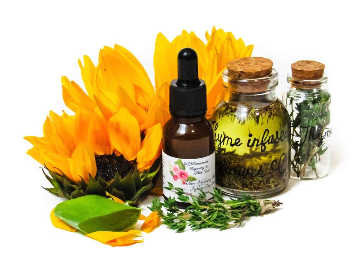 A bottle of JBHomemade Sugaring and Skin Care's Thyme Sunflower Harmony Nourishing Thyme-Infused Sunflower & Aloe Facial Serum is shown from an angled front view. Next to the bottle are the fresh ingredients that make up the serum: sunflower blossoms, a slice of aloe vera, a cork glass bottle of sunflower oil infused with thyme, and a cork glass bottle of fresh thyme sprigs.