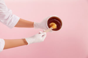 An aesthetician reaches into a tub of sugaring paste using an applicator, expertly preparing the ball of sugar for hair removal.