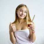 A woman holding up a jar of sugaring paste in her right hand and giving a thumbs up with her left.