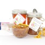 A bundle featuring an 8 oz mason jar of softer consistency sugaring wax, paired with a jar of Lemon Zest Cane Sugar Body Scrub. and Colloidal Oatmeal Brown Sugar Dry Body Scrub, a small bottle of pure aloe vera, a pouch of cornstarch, denim strips, an applicator, with a spilled jar of dried lemon zest and a bowl of the body scrub adorned with a lemon slice.