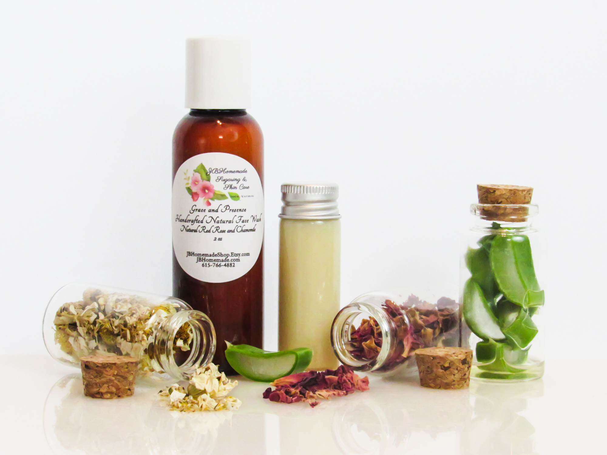 A front view of an all-natural facial cleanser in an amber bottle surrounded by small, corked glass bottles containing sprinkles of Red Rose, Aloe Vera and Chamomile ingredients. A clear glass bottle showcases the face wash's color and texture.