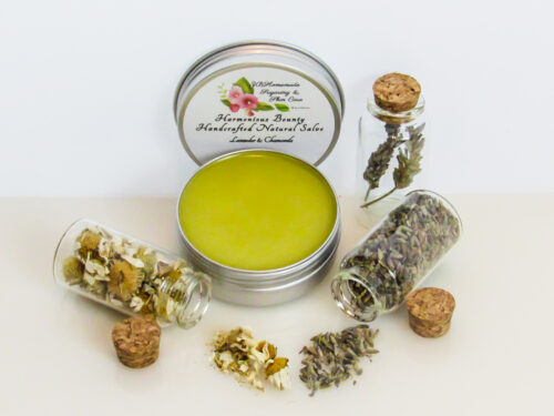 Harmonious Bounty presents its Creamy Natural Skin Salve in Lavender Chamomile, providing a comforting solution for dry skin. The product is showcased in an overhead view of an open tin, with its lid placed behind revealing the label. Encircling the salve are petite corked glass bottles filled with Lavender and Chamomile, accompanied by sprinkles of these soothing ingredients.