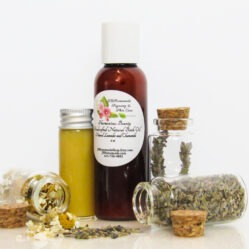A front, right angled view of an all-natural bath oil in an amber bottle surrounded by small, corked glass bottles containing Lavender and Chamomile ingredients and sprinkles of the same. A clear glass bottle showcases the bath oil's color and texture.