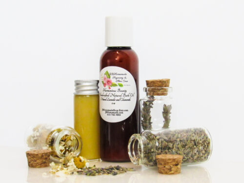 A front, right angled view of an all-natural bath oil in an amber bottle surrounded by small, corked glass bottles containing Lavender and Chamomile ingredients and sprinkles of the same. A clear glass bottle showcases the bath oil's color and texture.