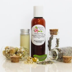 A front view of an all-natural facial cleanser in an amber bottle surrounded by small, corked glass bottles containing Lavender, Aloe Vera and Chamomile ingredients and sprinkles of the same. A clear glass bottle showcases the face wash's color and texture.