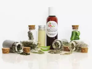Lake House Pine, Cedarwood, Spearmint, and Lavender Aloe Vera Face Wash Front perspective view of an all-natural facial cleanser in an amber bottle surrounded by six small, corked glass bottles containing sprinkles of pine, cedarwood, spearmint, and lavender ingredients. A clear glass bottle showcases the face wash’s color and texture.