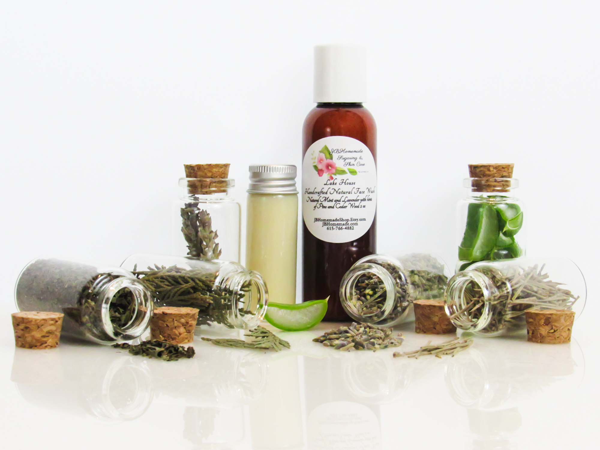 Front perspective view of an all-natural facial cleanser in an amber bottle surrounded by six small, corked glass bottles containing sprinkles of pine, cedarwood, spearmint, and lavender ingredients. A clear glass bottle showcases the face wash’s color and texture.