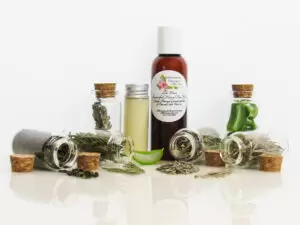 Front perspective view of an all-natural facial cleanser in an amber bottle surrounded by six small, corked glass bottles containing sprinkles of pine, cedarwood, spearmint, and lavender ingredients. A clear glass bottle showcases the face wash’s color and texture.