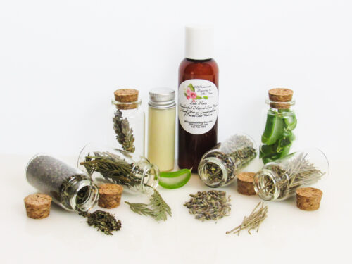Front View of an all-natural facial cleanser in an amber bottle surrounded by six small, corked glass bottles containing sprinkles of pine, cedarwood, spearmint, and lavender ingredients. A clear glass bottle showcases the face wash’s color and texture.