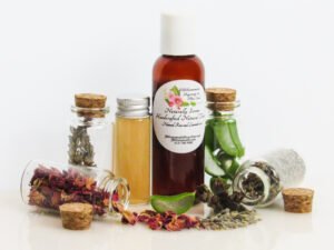 Naturally Serene Lavender and Red Rose Toner in an amber bottle, surrounded by organic ingredients like aloe vera slices, dried lavender sprigs, witch hazel, and red rose petals on a white surface.