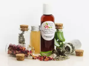 Naturally Serene Lavender & Rose Infused Natural Toner with Fresh Ingredients Displayed Naturally Serene Lavender and Red Rose Toner in an amber bottle, surrounded by organic ingredients like aloe vera slices, dried lavender sprigs, witch hazel, and red rose petals on a white surface.