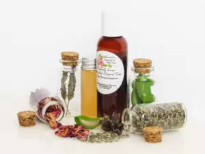 Naturally Serene Lavender and Red Rose Toner in an amber bottle, surrounded by organic ingredients like aloe vera slices, dried lavender sprigs, witch hazel, and red rose petals on a white surface.