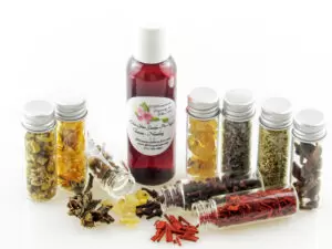 A bottle of Adorn Your Garden Sugaring Cleanser and Prep surrounded by small jars containing its all-natural ingredients like Chamomile, Calendula, Frankincense, Clove, Sandalwood, Lavender, Rosemary, and Ylang Ylang Extra. Front view.