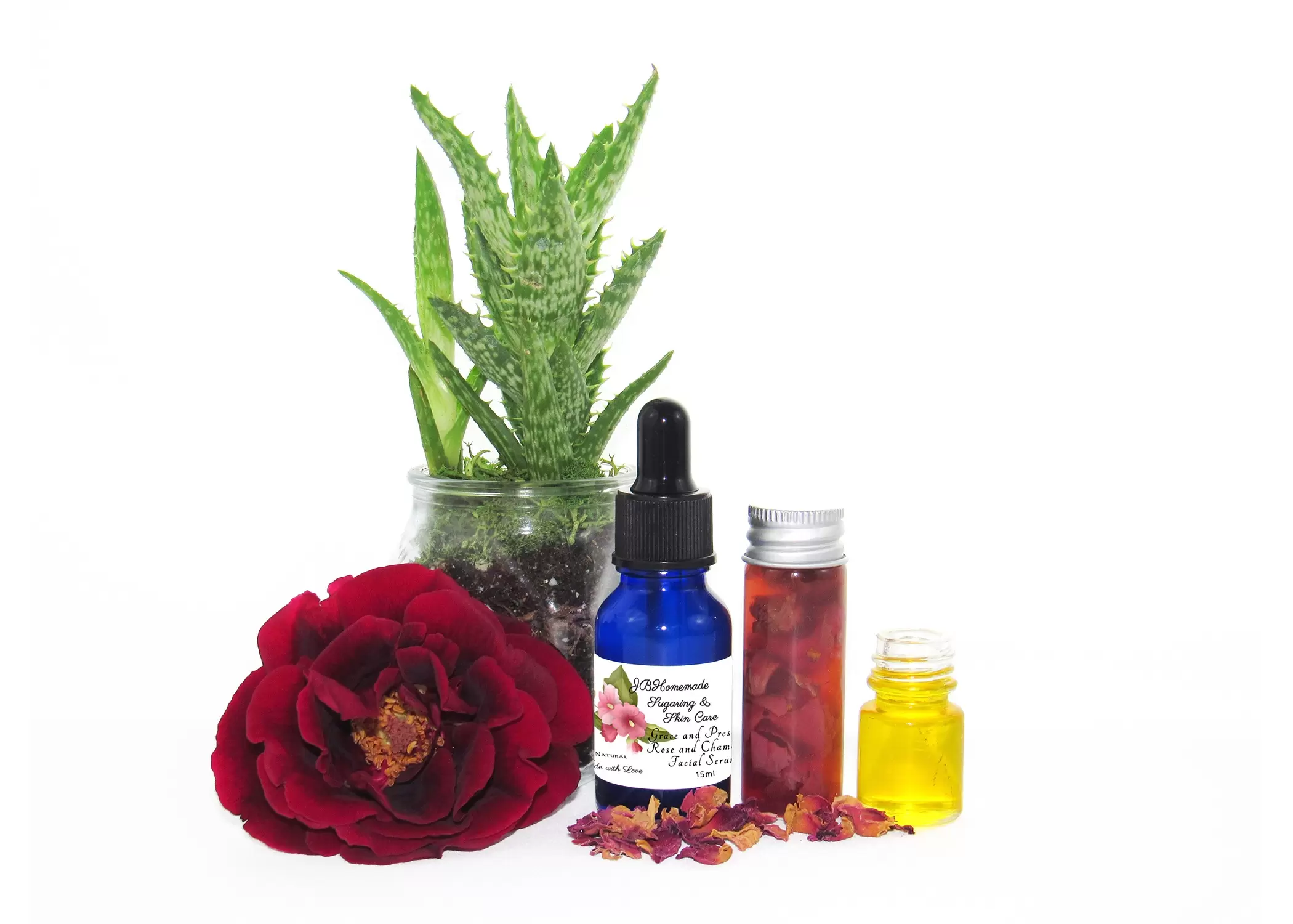 A cobalt blue bottle of Grace and Presence Rose and Chamomile Facial Serum, accompanied by its natural ingredients including aloe vera, rose, and chamomile-infused grapeseed oil.