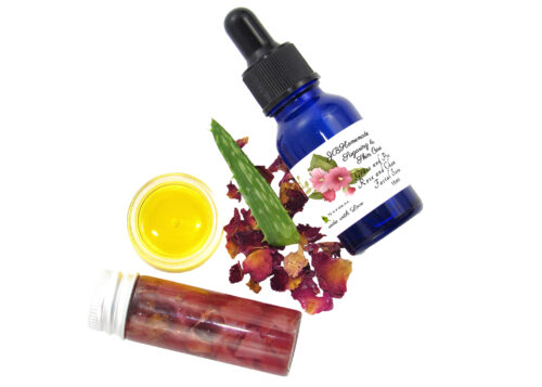 A cobalt bottle of Grace and Presence Serum, rose-infused aloe vera in a glass bottle, and rose & chamomile-infused grapeseed oil showcased with dried roses and an aloe leaf.