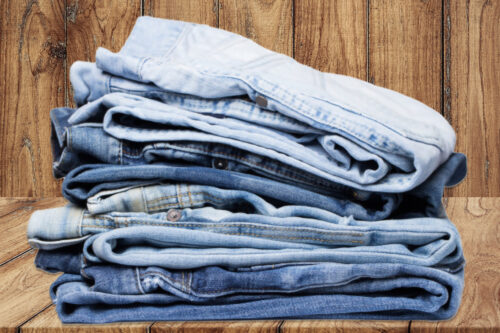A neatly stacked pile of denim material showcasing various shades and textures, used in making denim strips for sugaring wax bundles.